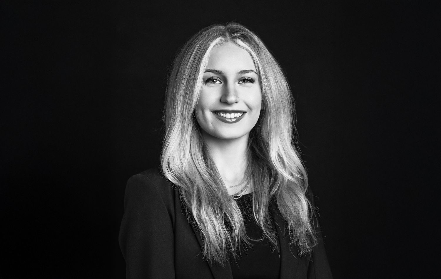 Professional studio headshot in black and white showing a confident expression against a dark background.