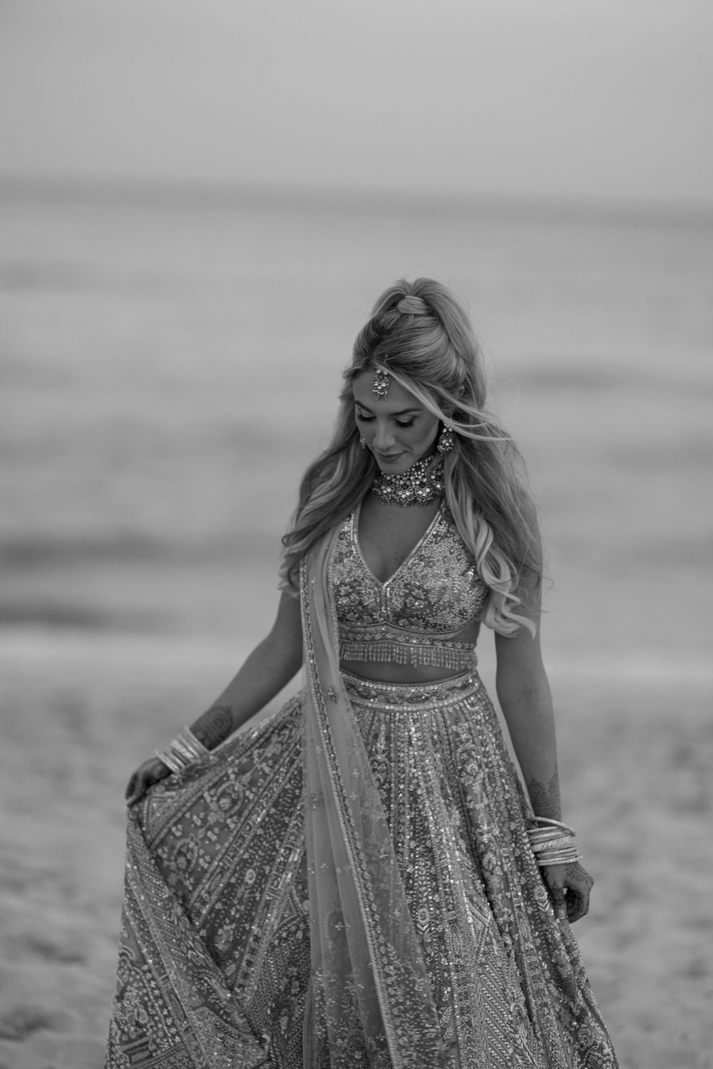 A black and white photograph showing someone in a textured empire waist gown twirling on a beach.