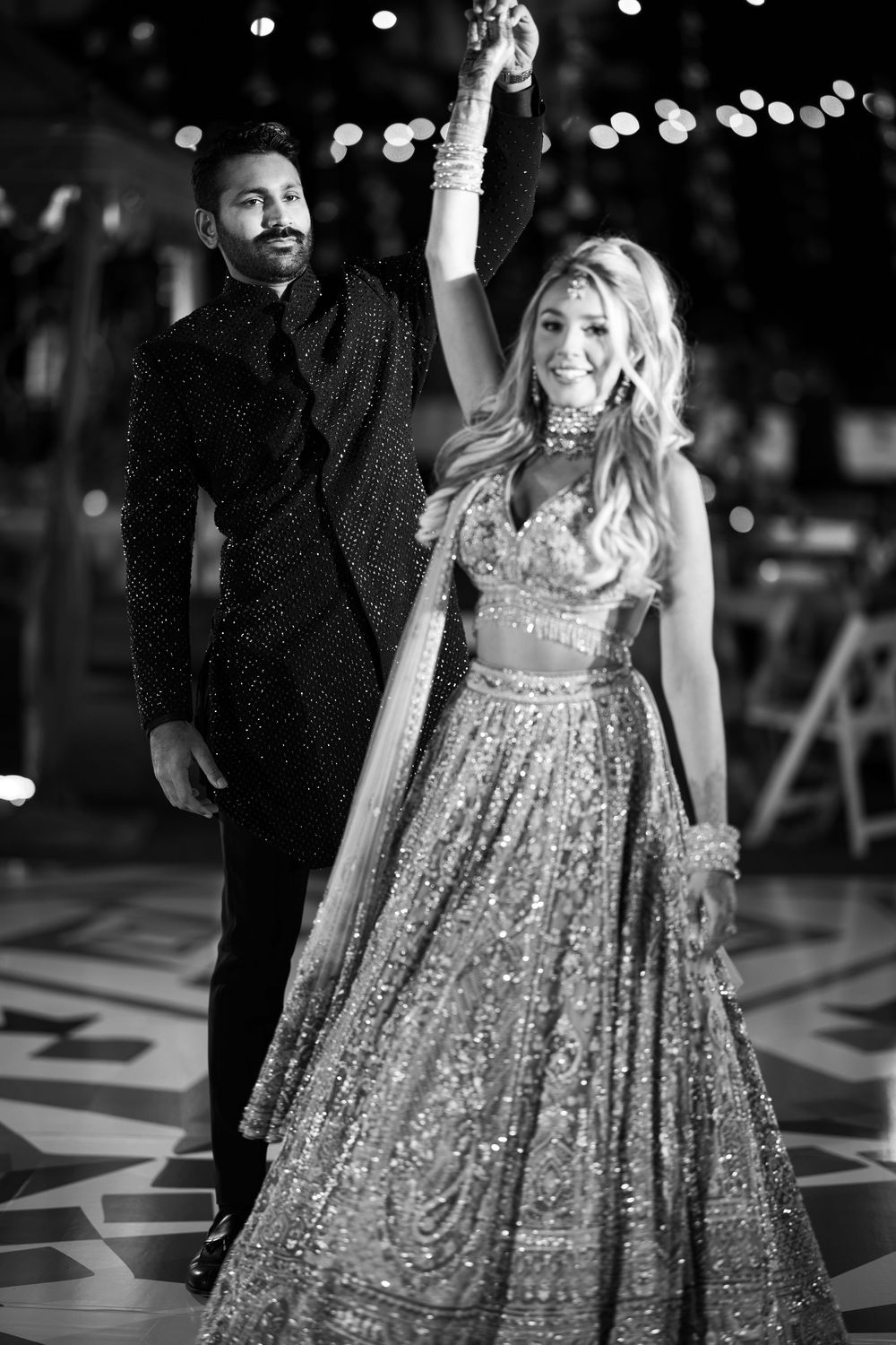 Couple in formal attire strike a dramatic pose on a patterned dance floor with bokeh lights.