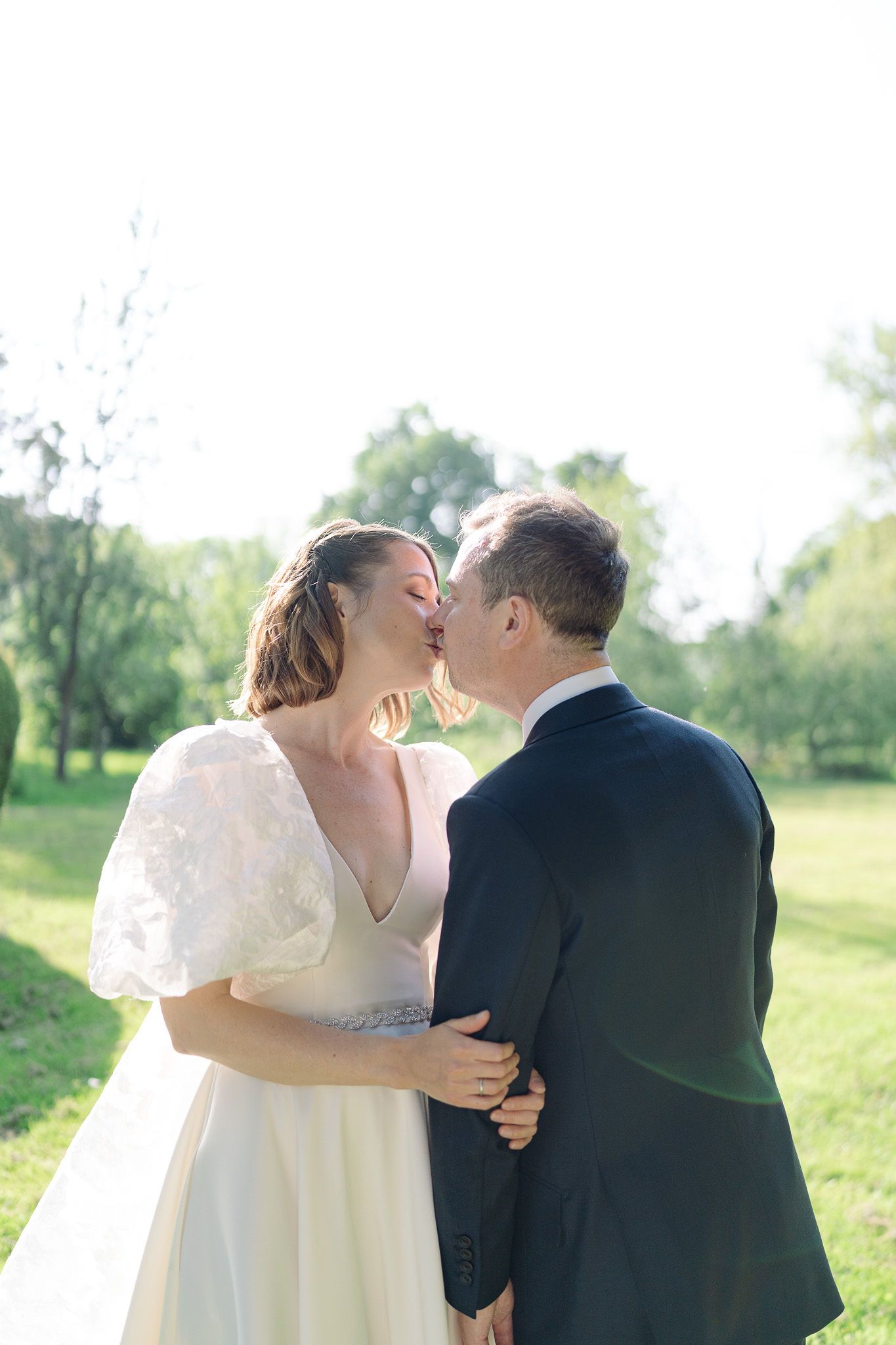 Wedding couple sharing a kiss in a sunlit garden setting.