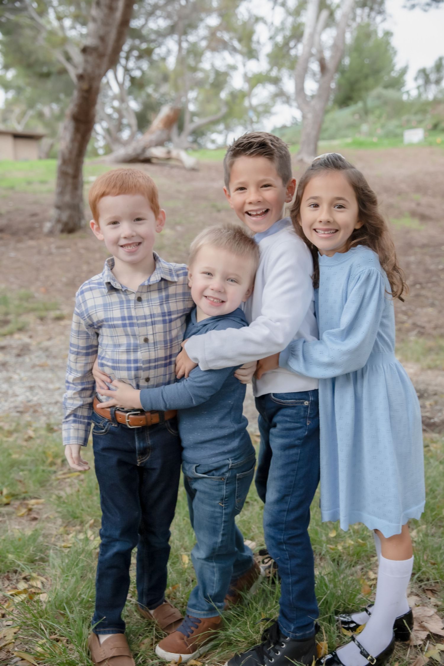 Four siblings in coordinating blue and plaid outfits pose playfully together outdoors.