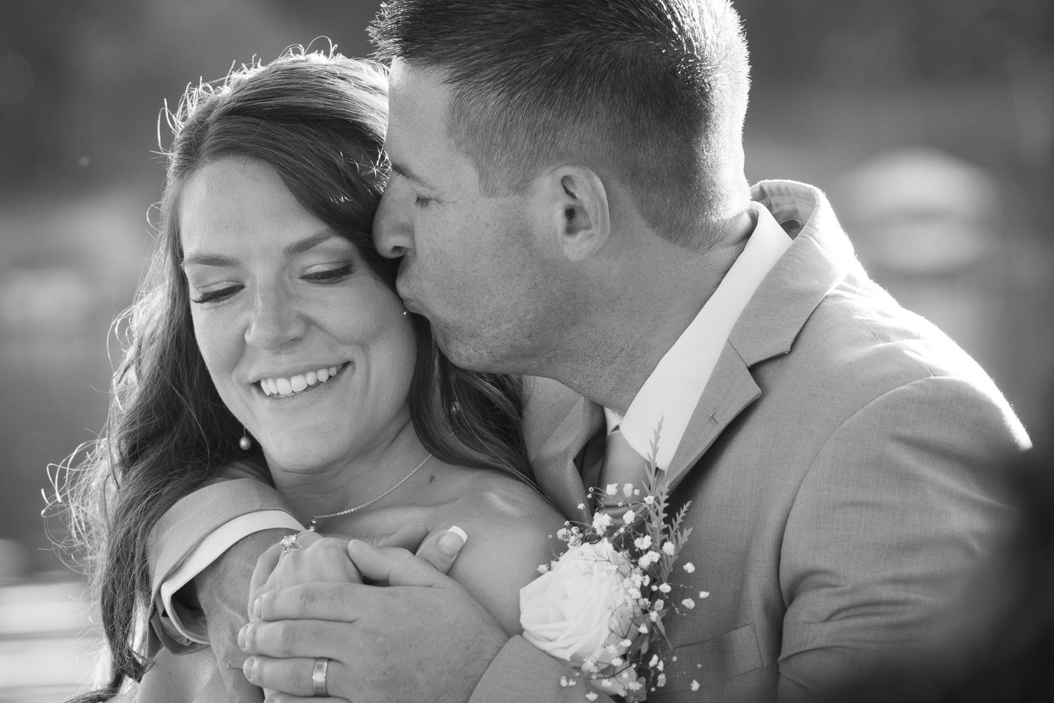 Black and white romantic candid wedding photo showing tender moment between couple with boutonniere and long hair.