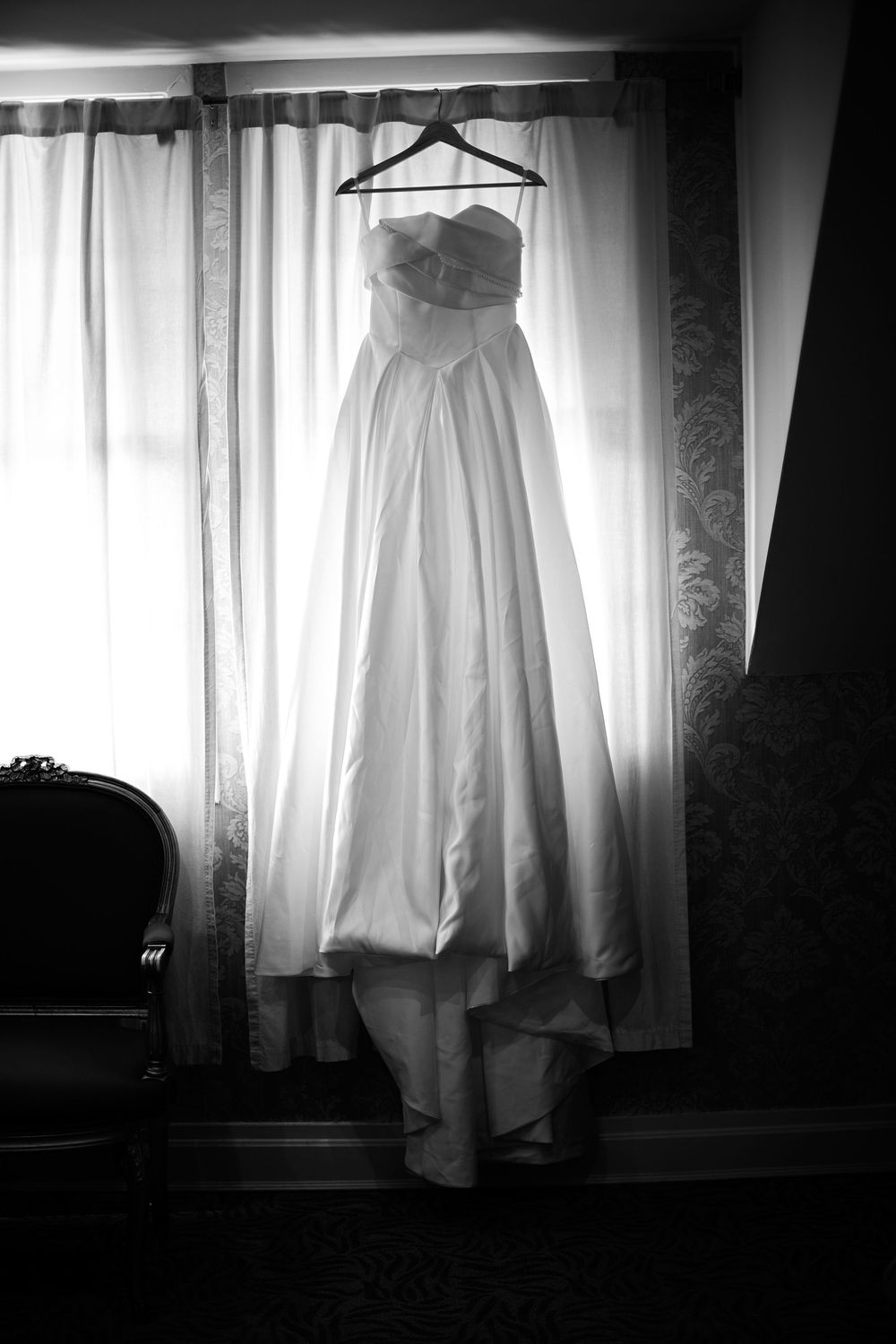 A moody black and white photograph series of a white wedding dress hanging by a sunlit window. at VIVO RESTAURANT