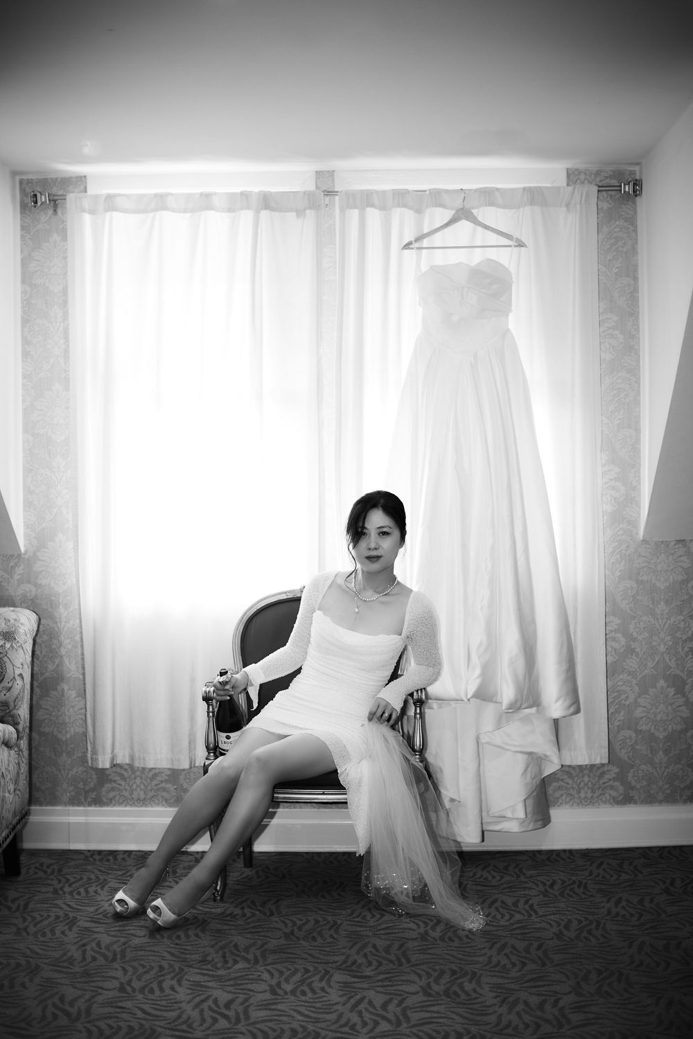 Black and white photo of bridal preparation room showing hanging wedding dress and arranged seating near window. at VIVO RESTAURANT