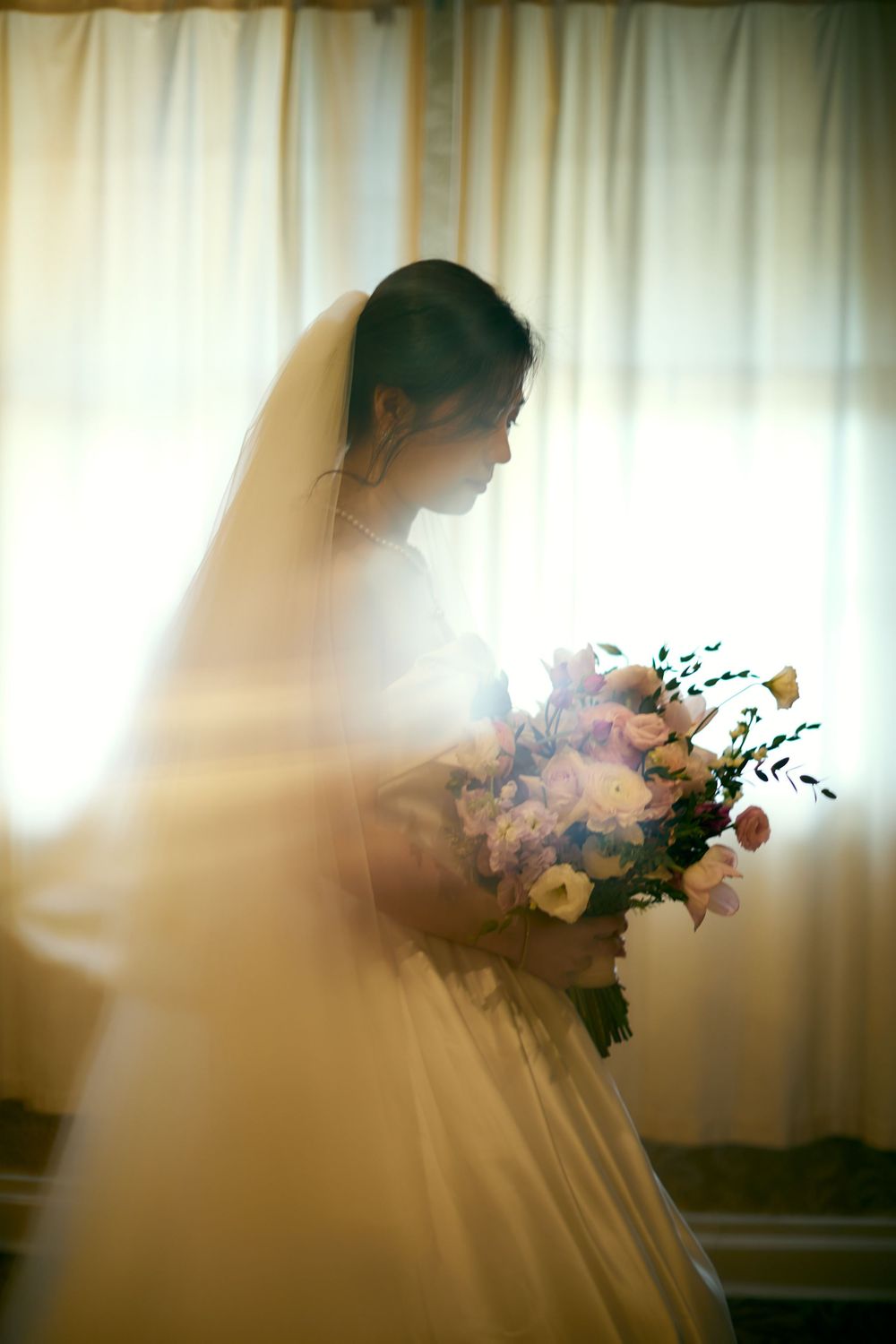 Ethereal silhouette of a bride in a flowing veil holding a romantic bouquet against sunlit curtains in a dreamy sequence. at VIVO RESTAURANT