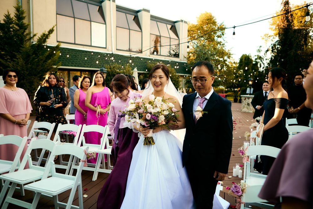 Wedding guests stand in line during an outdoor reception with white chairs and pink floral decorations at sunset. at VIVO RESTAURANT