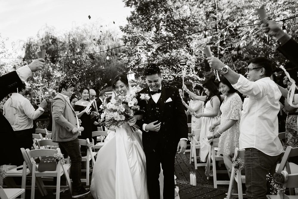 Wedding guests celebrate with bubbles as newlyweds walk down the aisle at an outdoor garden ceremony. at VIVO RESTAURANT