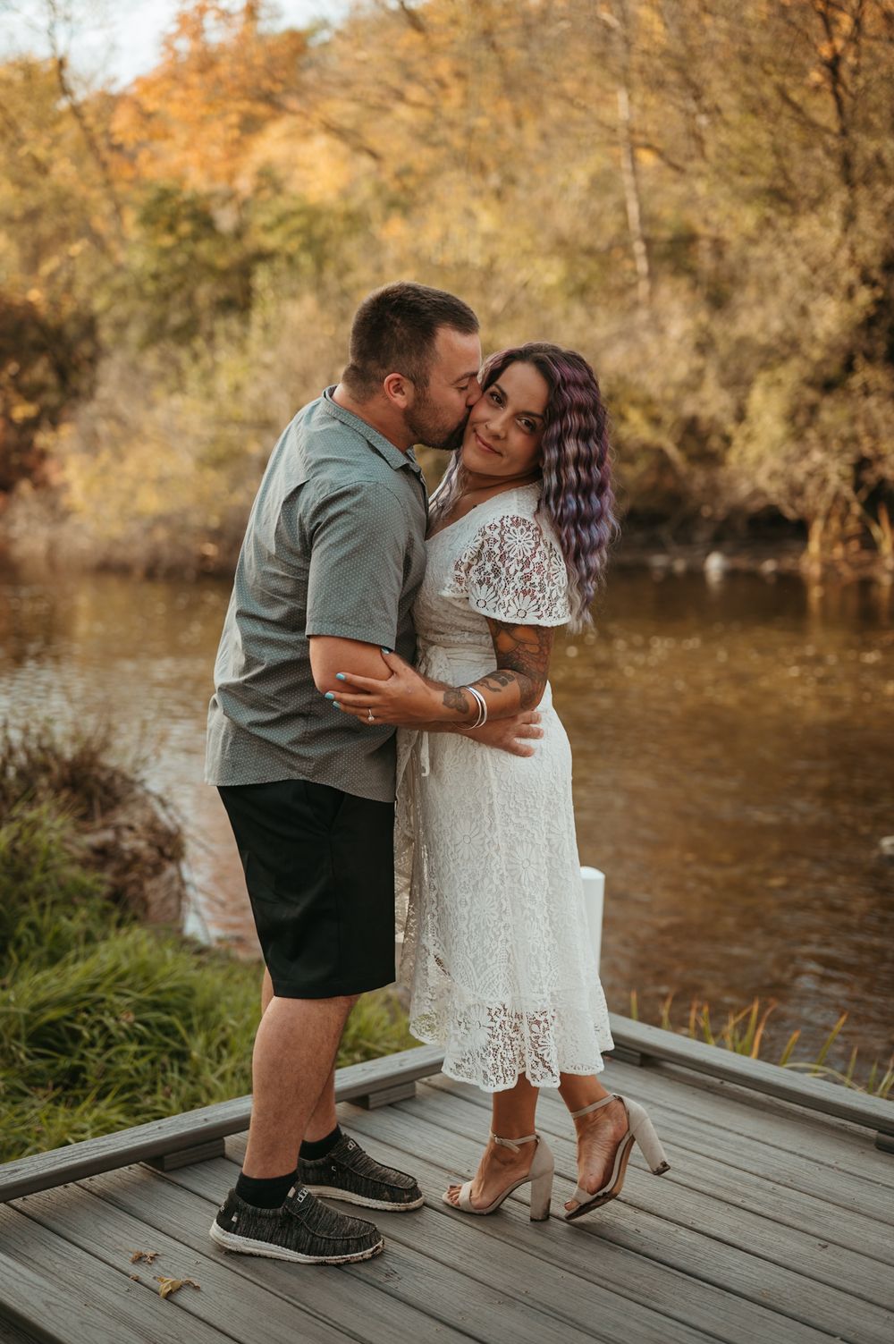 Couple shares tender moments on a wooden dock by an autumn lake in a series of romantic photos.