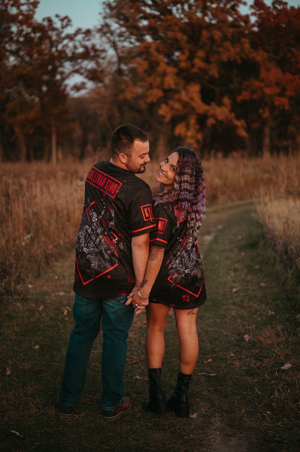 A couple standing on a dirt path in autumn scenery share an intimate moment in matching printed shirts.