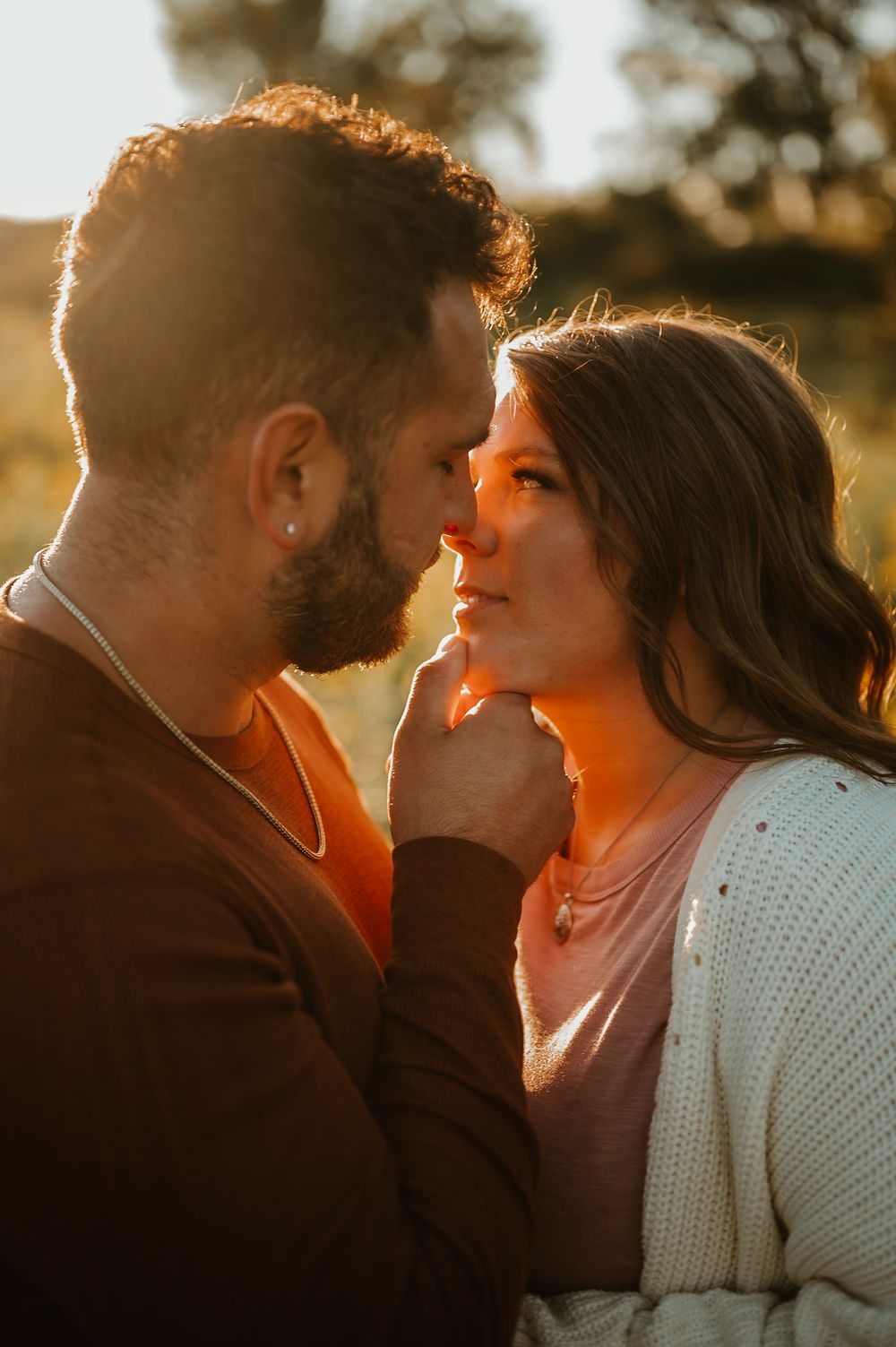 Romantic couple sharing an intimate moment in golden sunset lighting with sun flare behind them.