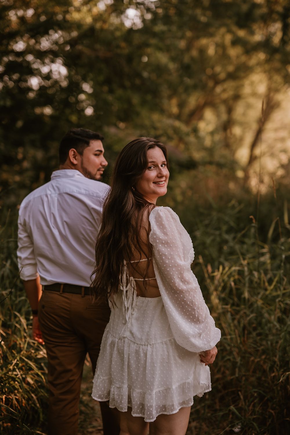 A couple embraces and laughs together in a natural outdoor setting during golden hour.