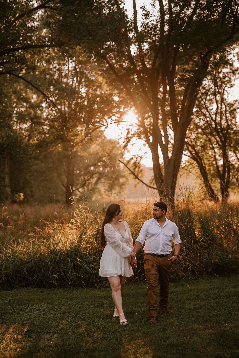 A sunset maternity session in a field with golden light filtering through trees as a couple shares intimate moments.
