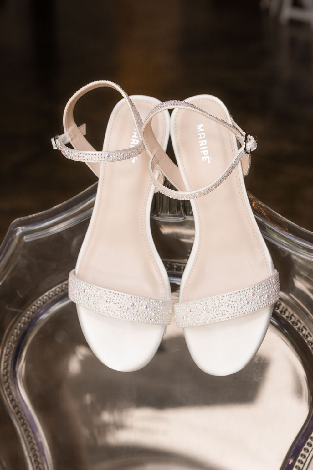 Delicate white baby shoes with ankle straps displayed on a clear glass surface.