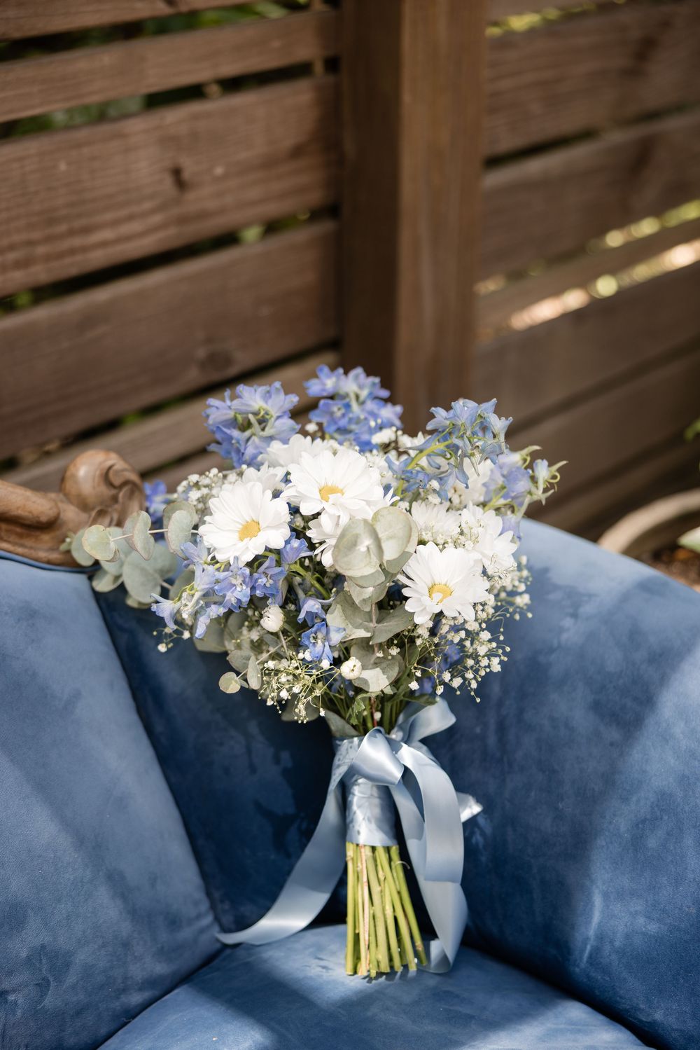 Elegant white and blue wedding bouquet resting on a navy blue velvet couch.