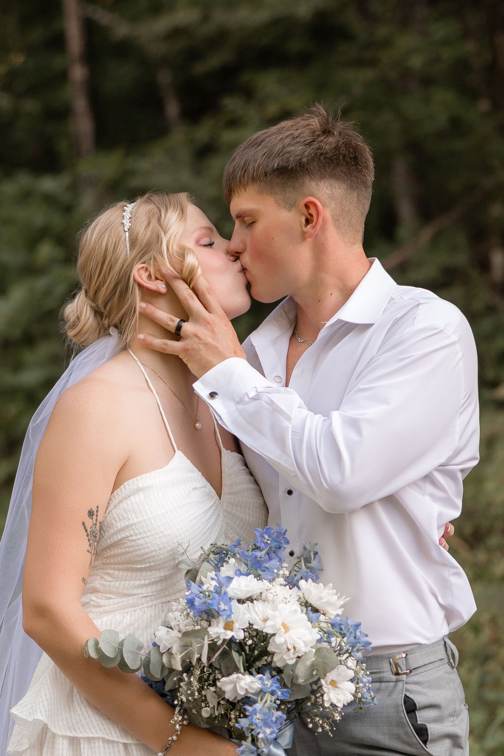A romantic moment captured at a wedding with delicate blue and white florals against a forest backdrop.