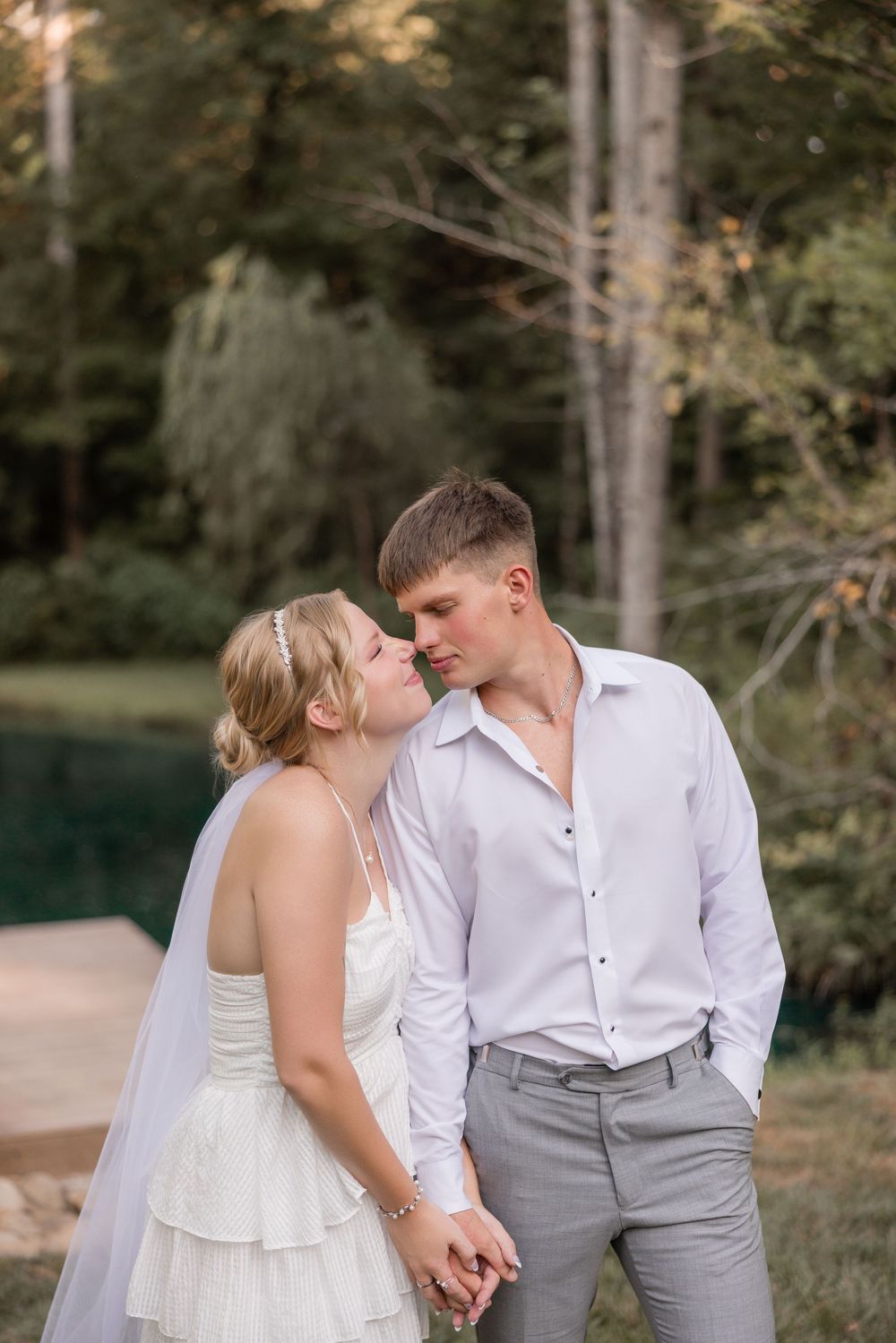 A couple in wedding attire shares intimate moments together in a wooded outdoor setting.