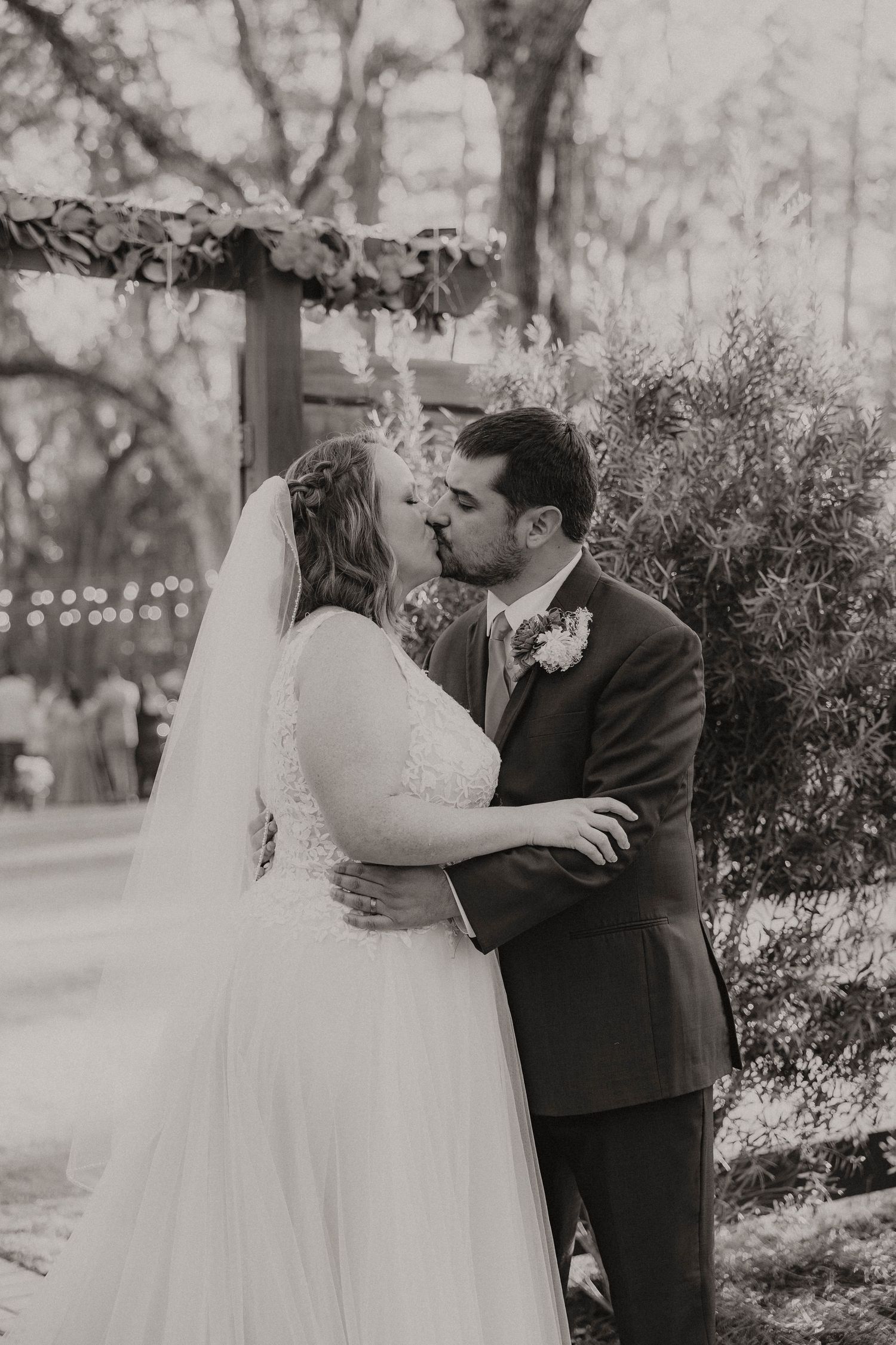 Romantic wedding couple sharing intimate moments while holding a floral bouquet outside a venue.