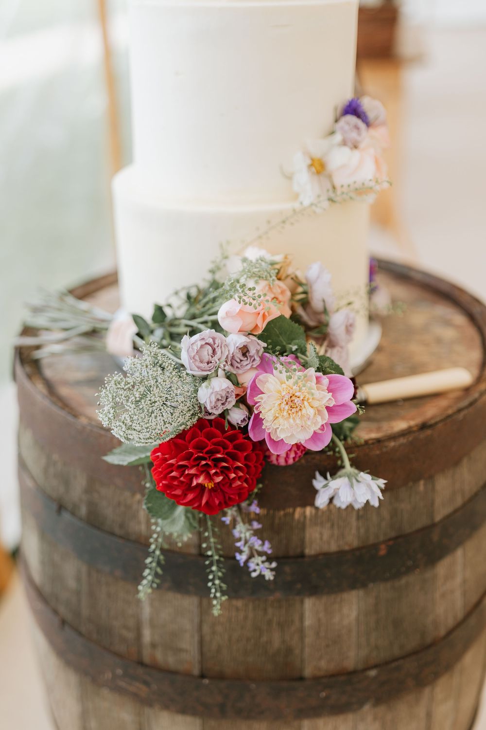 A rustic wooden barrel top decorated with delicate pink and red flowers and greenery arranged in a floral centerpiece.