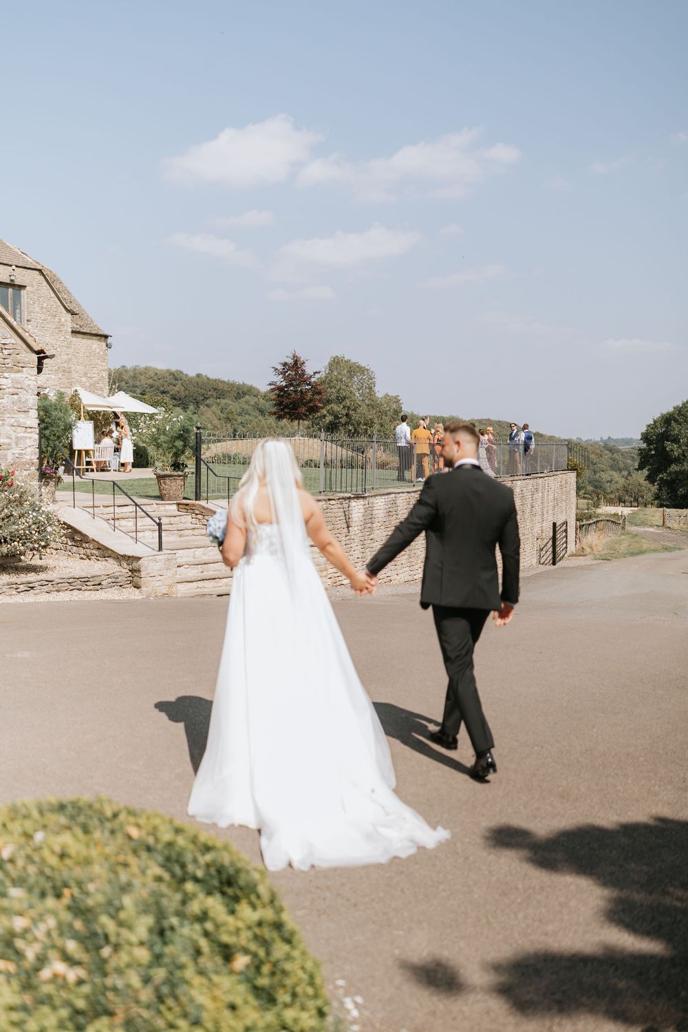 Bride and groom walking hand in hand at outdoor wedding venue on sunny day.
