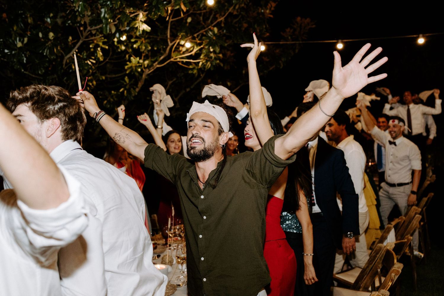 Crowd of wedding guests dancing with hands raised during an energetic celebration.