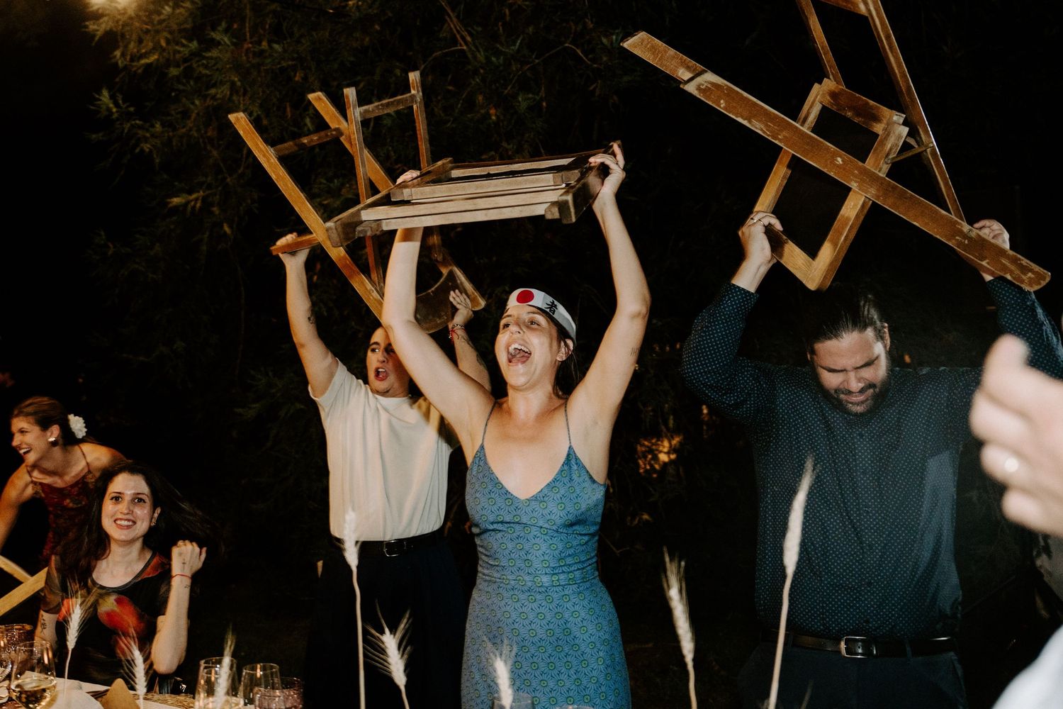 Party guests dancing with raised arms under string lights at an outdoor evening celebration.