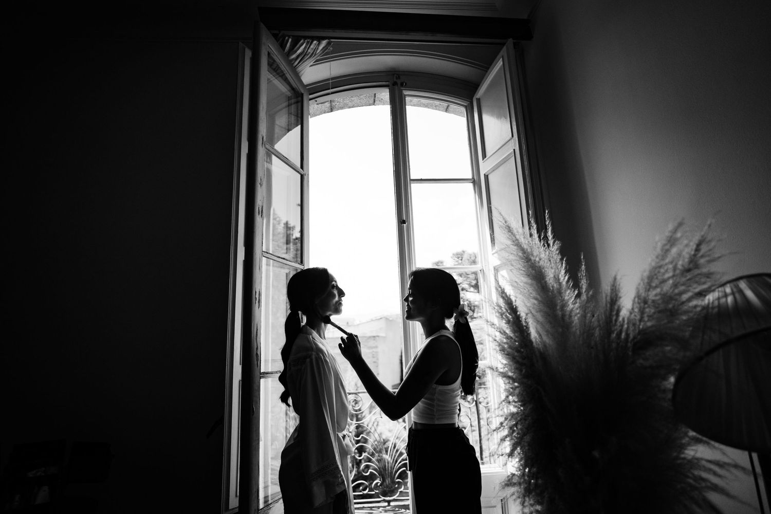 Artistic black and white silhouette of two figures standing by a bright window.