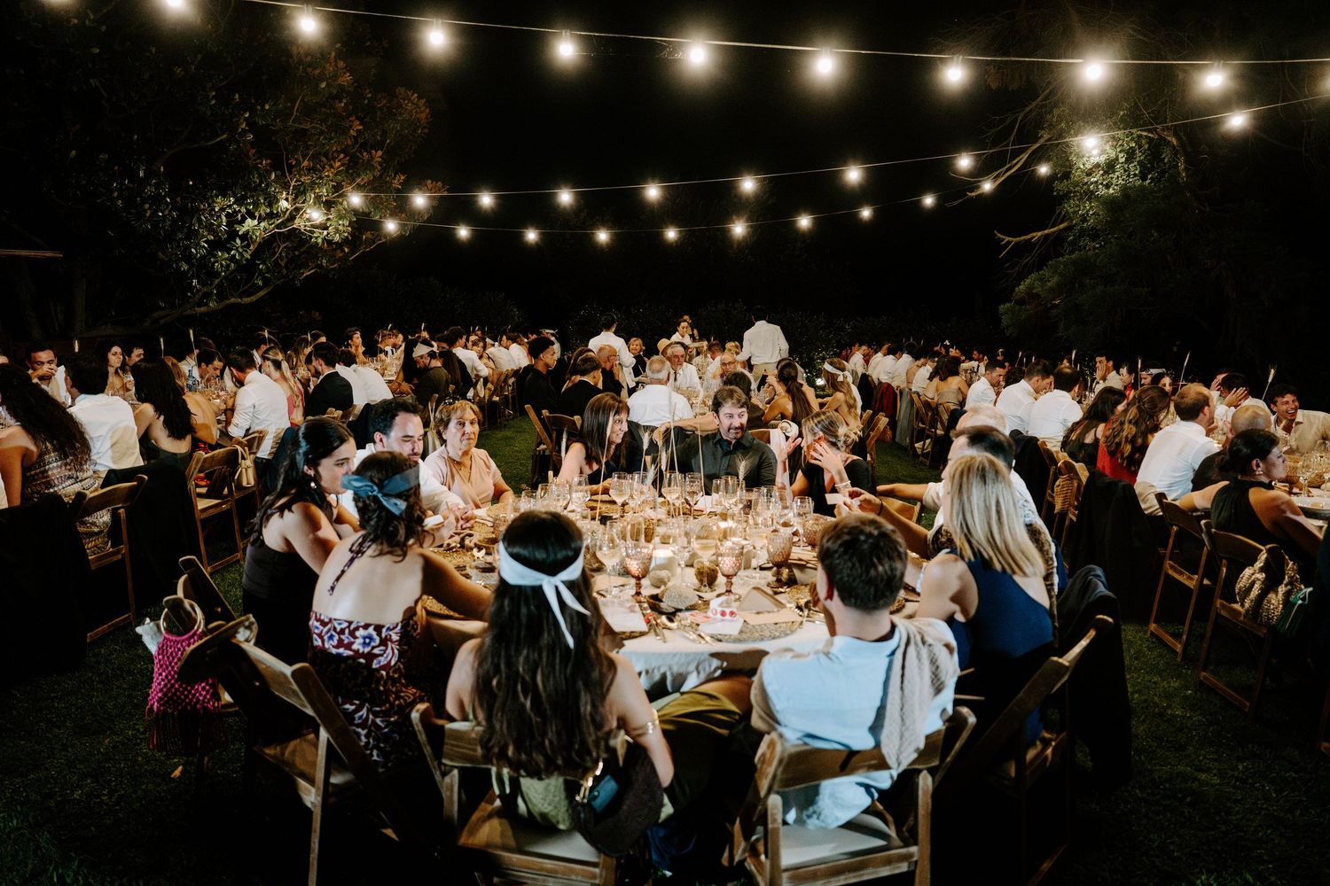String lights illuminate an outdoor wedding reception setting creating a magical atmosphere.