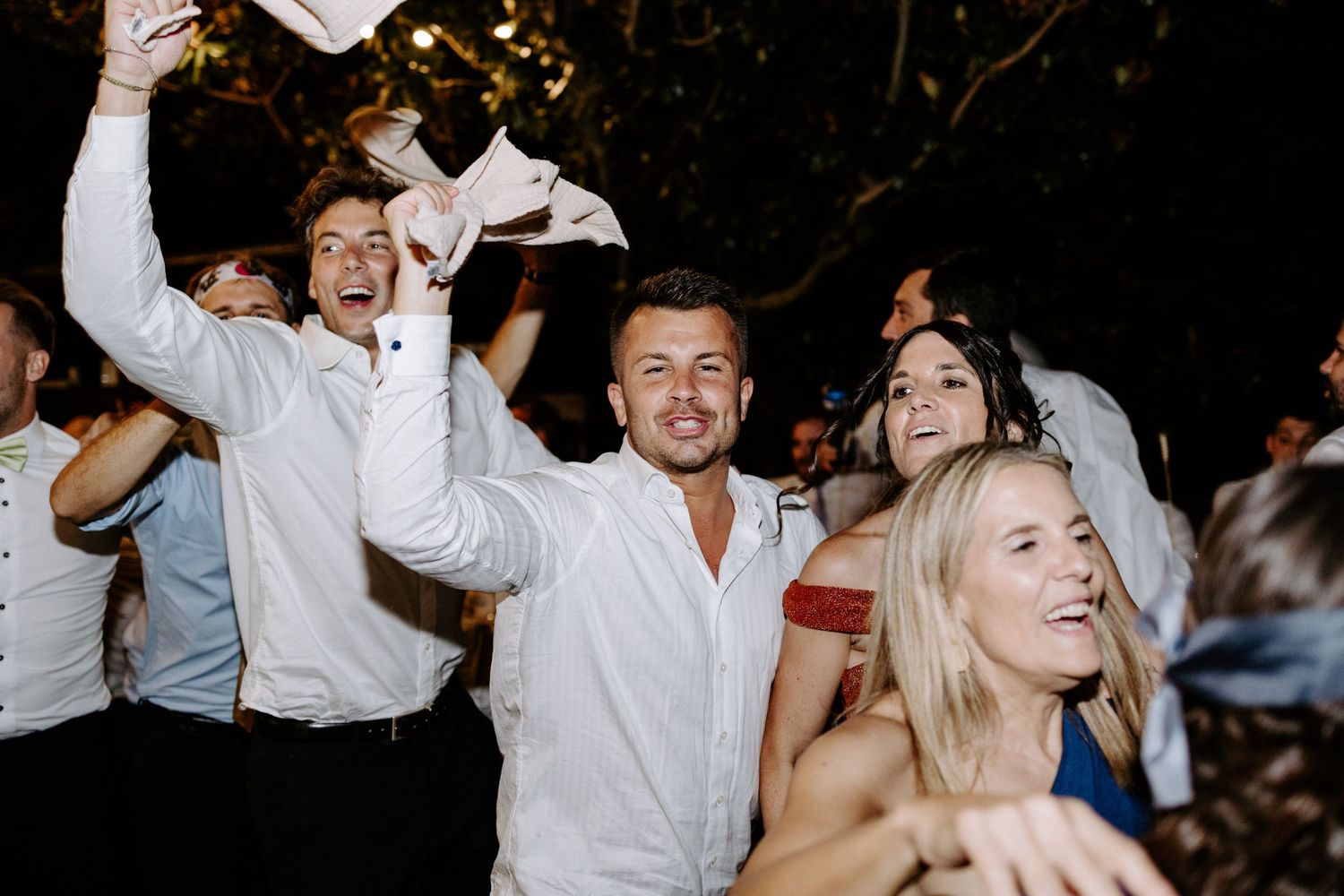 Guests dancing enthusiastically at a nighttime wedding celebration with dramatic lighting.