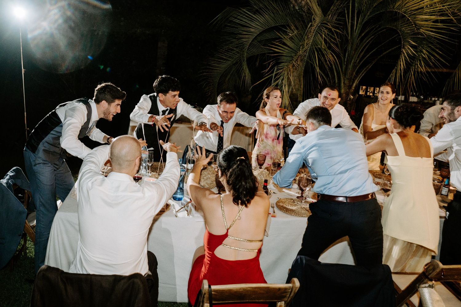 Wedding party dancing energetically during reception under bright lights.