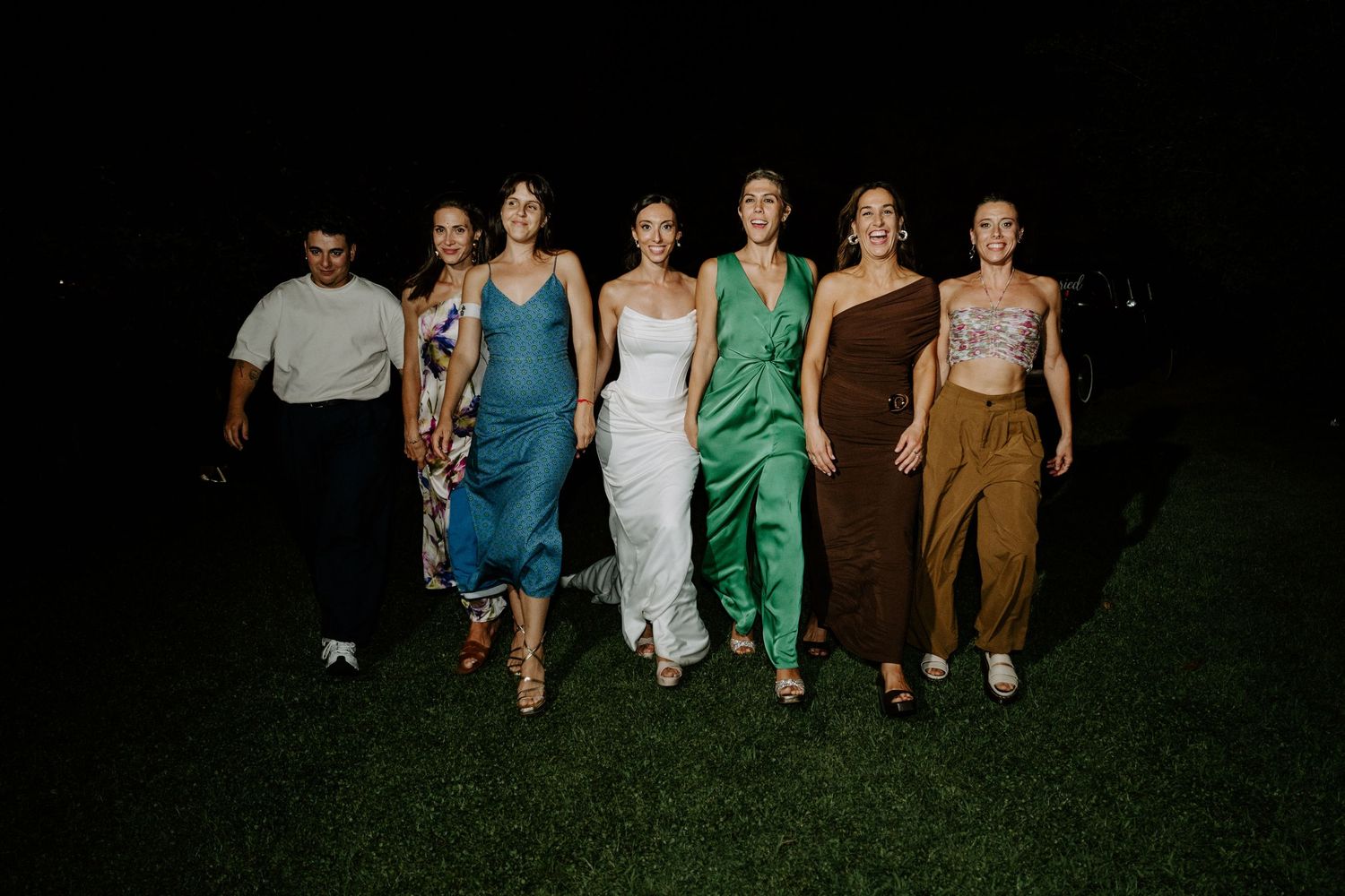 Group walking together at night wearing colorful formal attire and dresses.