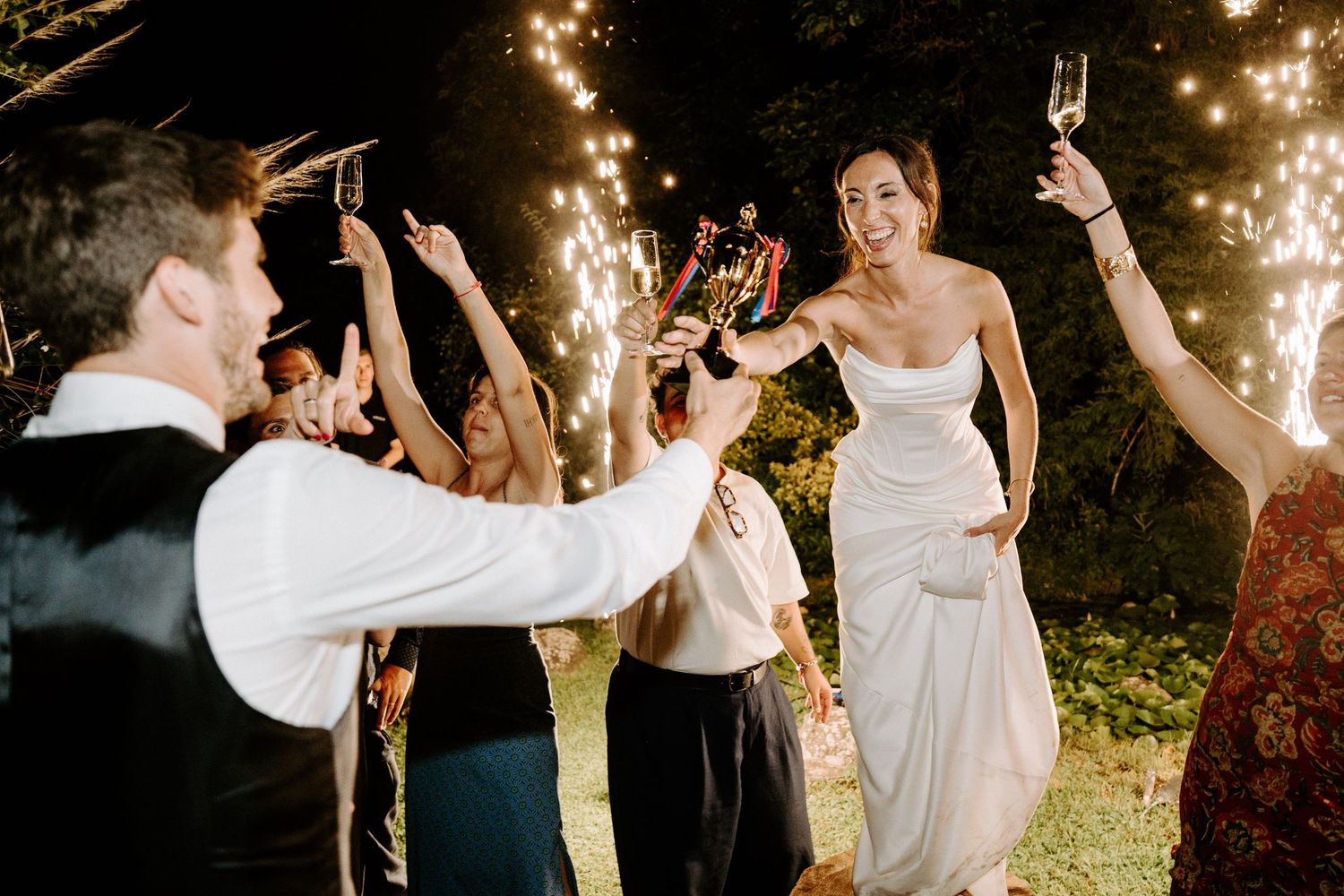 Wedding celebration with guests raising glasses for a toast outdoors at night.