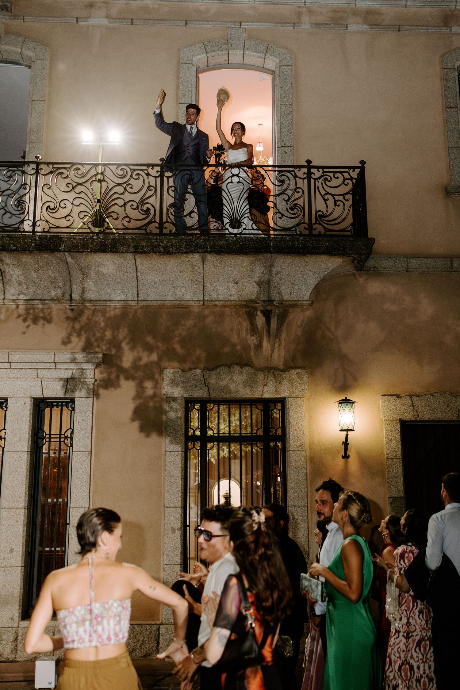 Wedding guests dancing below while others celebrate on ornate balcony of historic building.