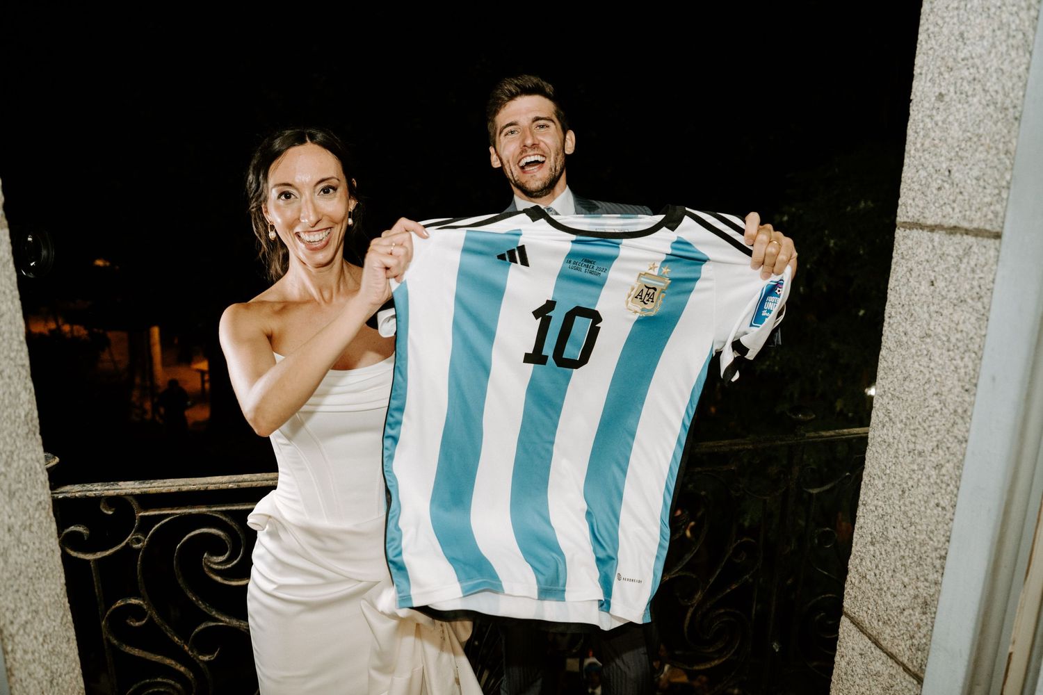 Wedding guests dance and celebrate on a balcony overlooking an outdoor venue at night.