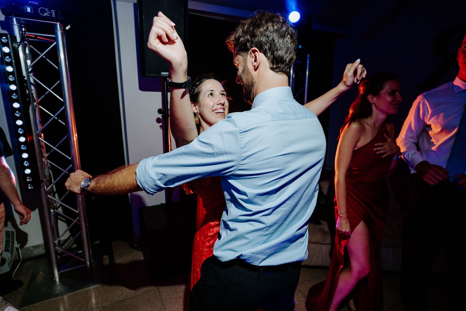 Wedding guests dancing under blue stage lighting at a reception party.