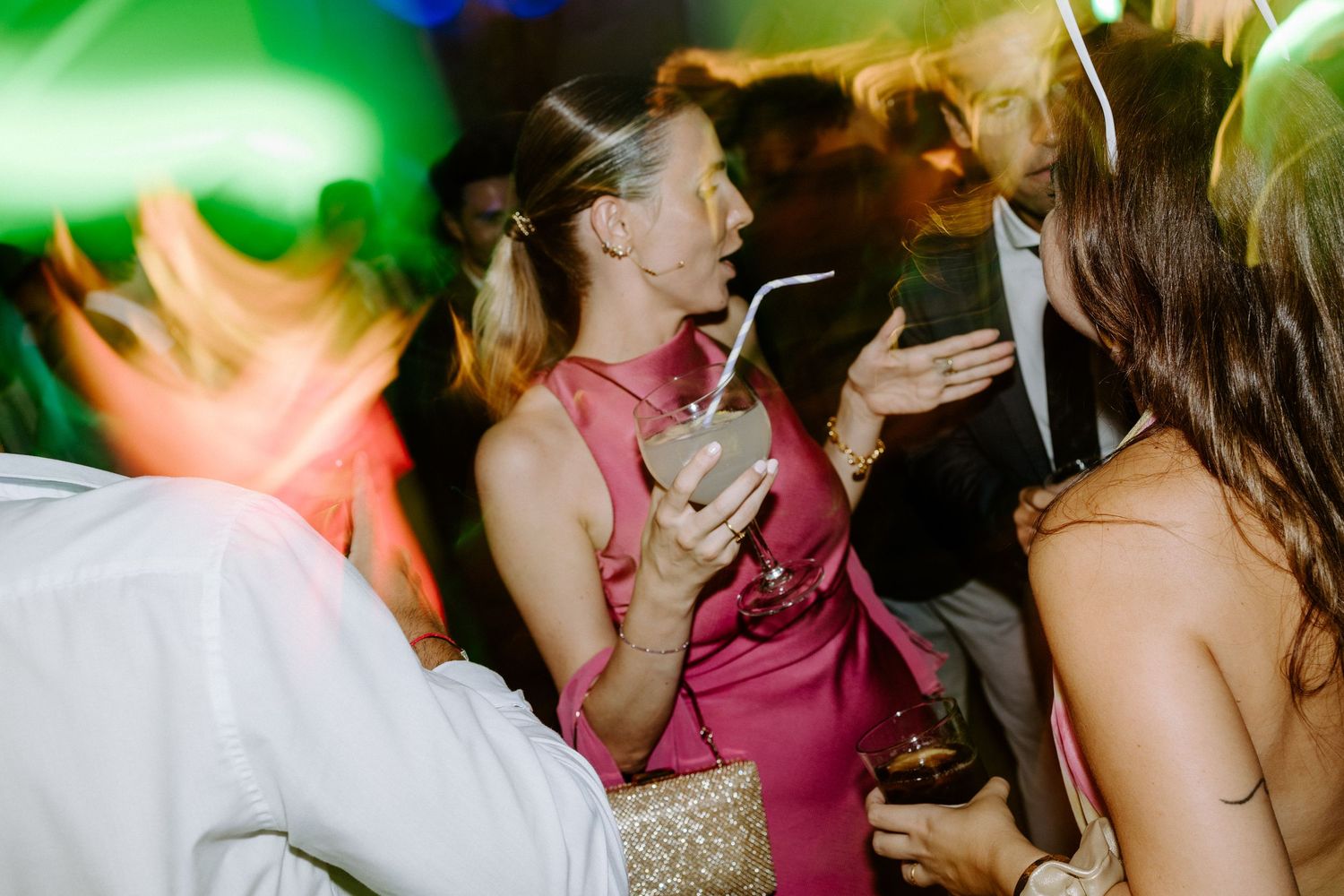 Wedding guests dancing under colorful lighting at a lively reception celebration.