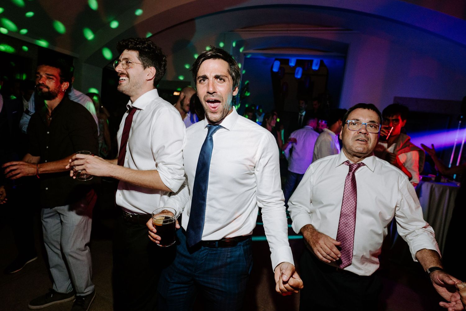Wedding guests dancing enthusiastically on a colorful dance floor with purple and green lighting.