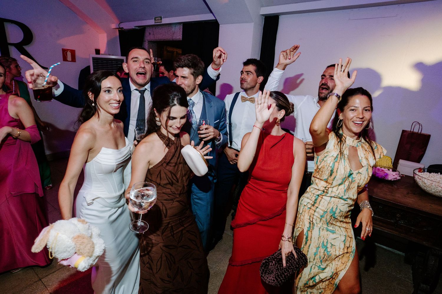 Energetic crowd dancing and celebrating at a lively party with purple mood lighting.