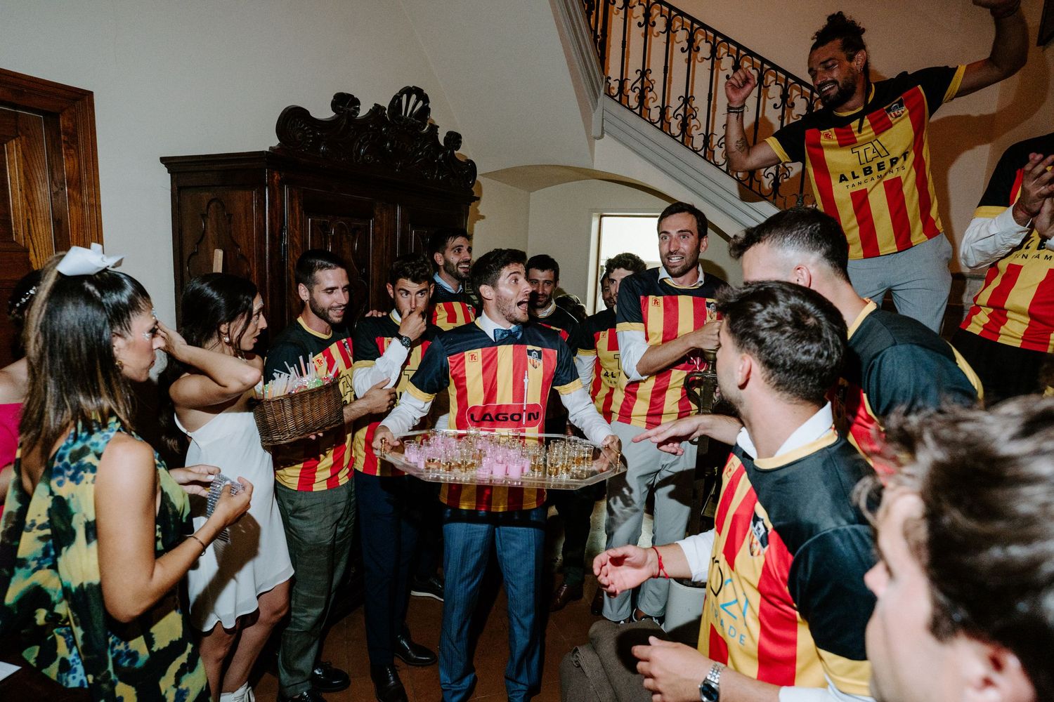 Party guests mingling and socializing in a crowded indoor venue with wooden staircase.