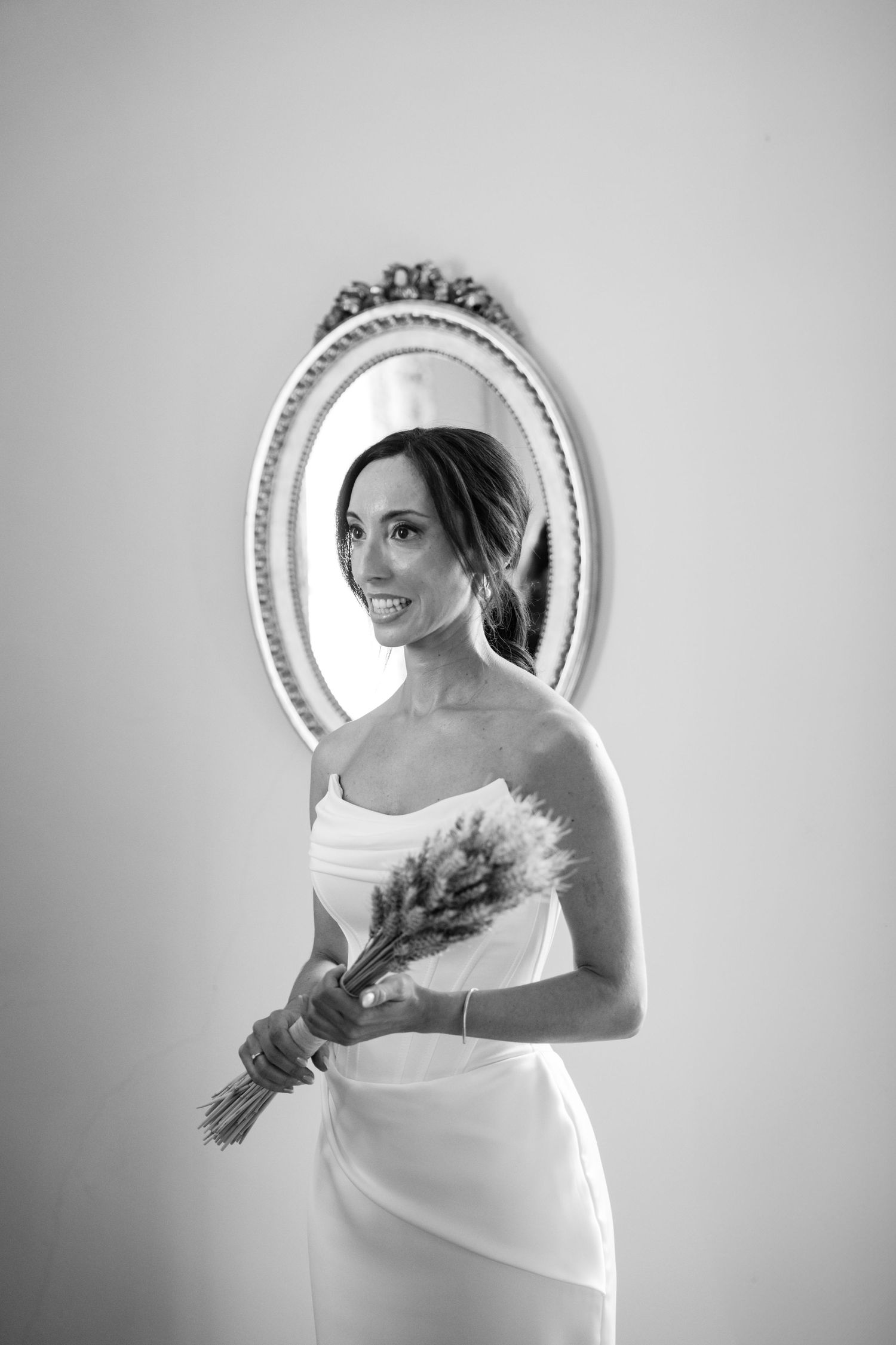 Black and white portraits of a bride with bouquet reflected in an ornate circular mirror.
