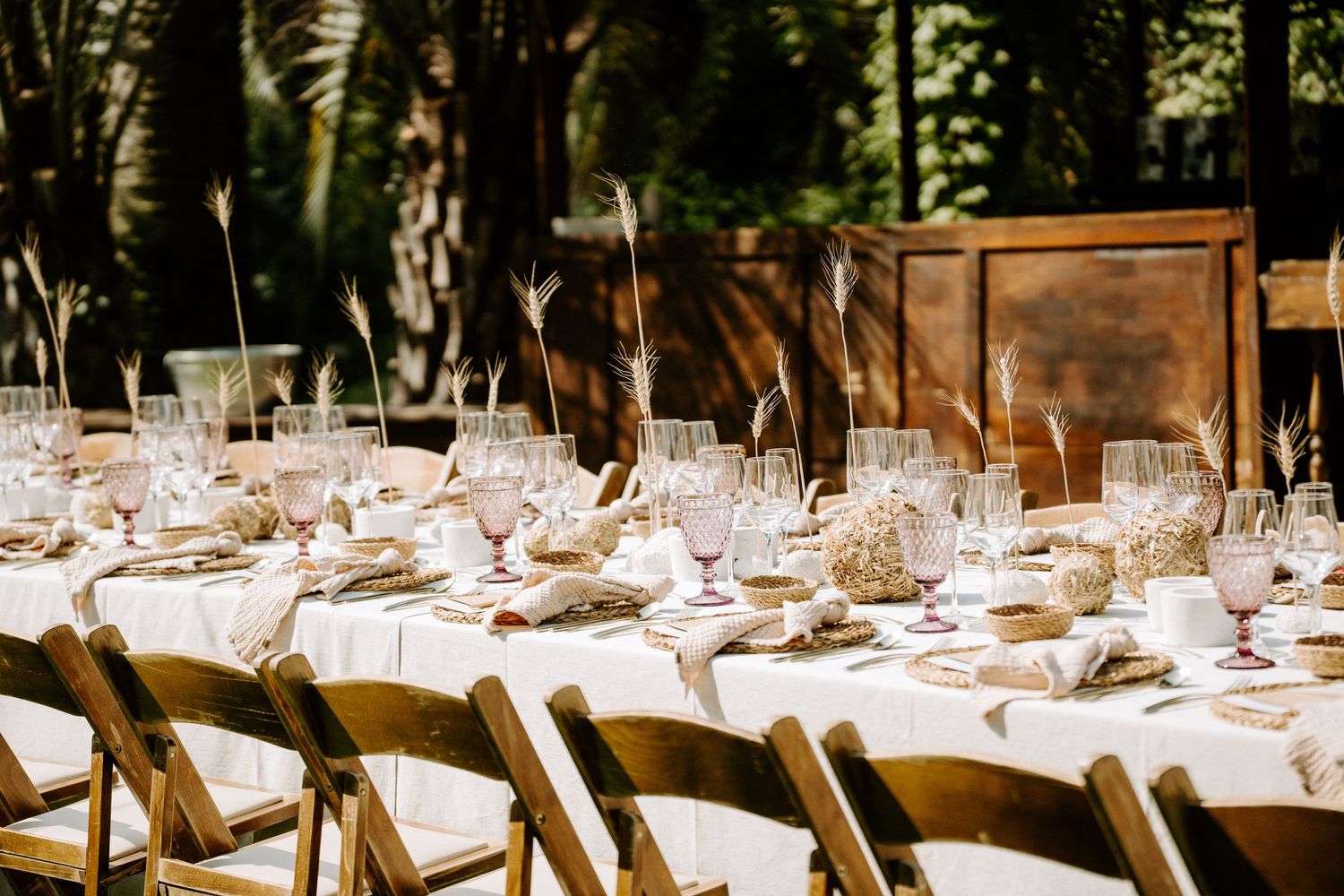 Rustic outdoor wedding reception tables set with elegant place settings under trees.