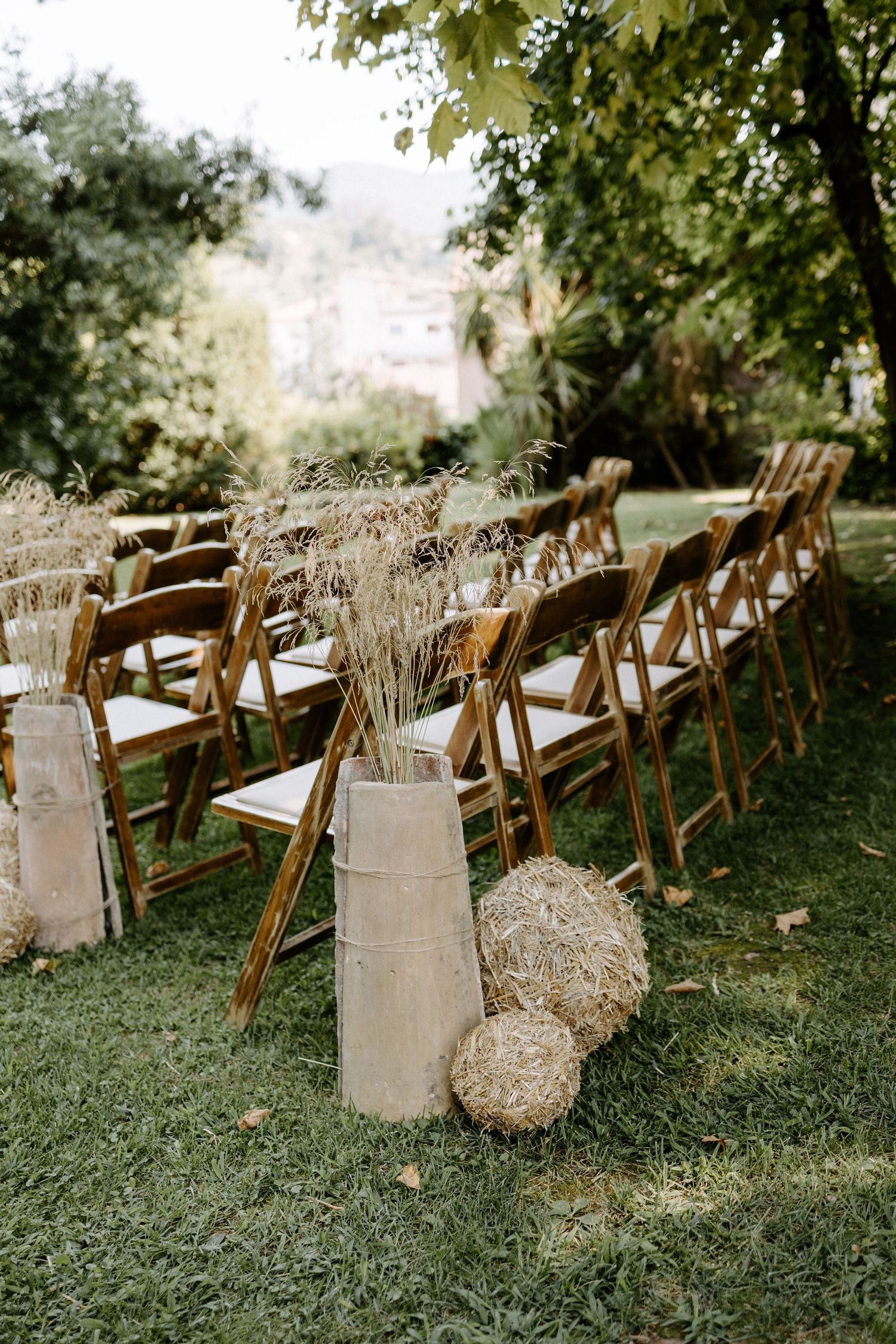 Rustic wedding ceremony setup with wooden chairs and dried wheat bundles along the aisle.
