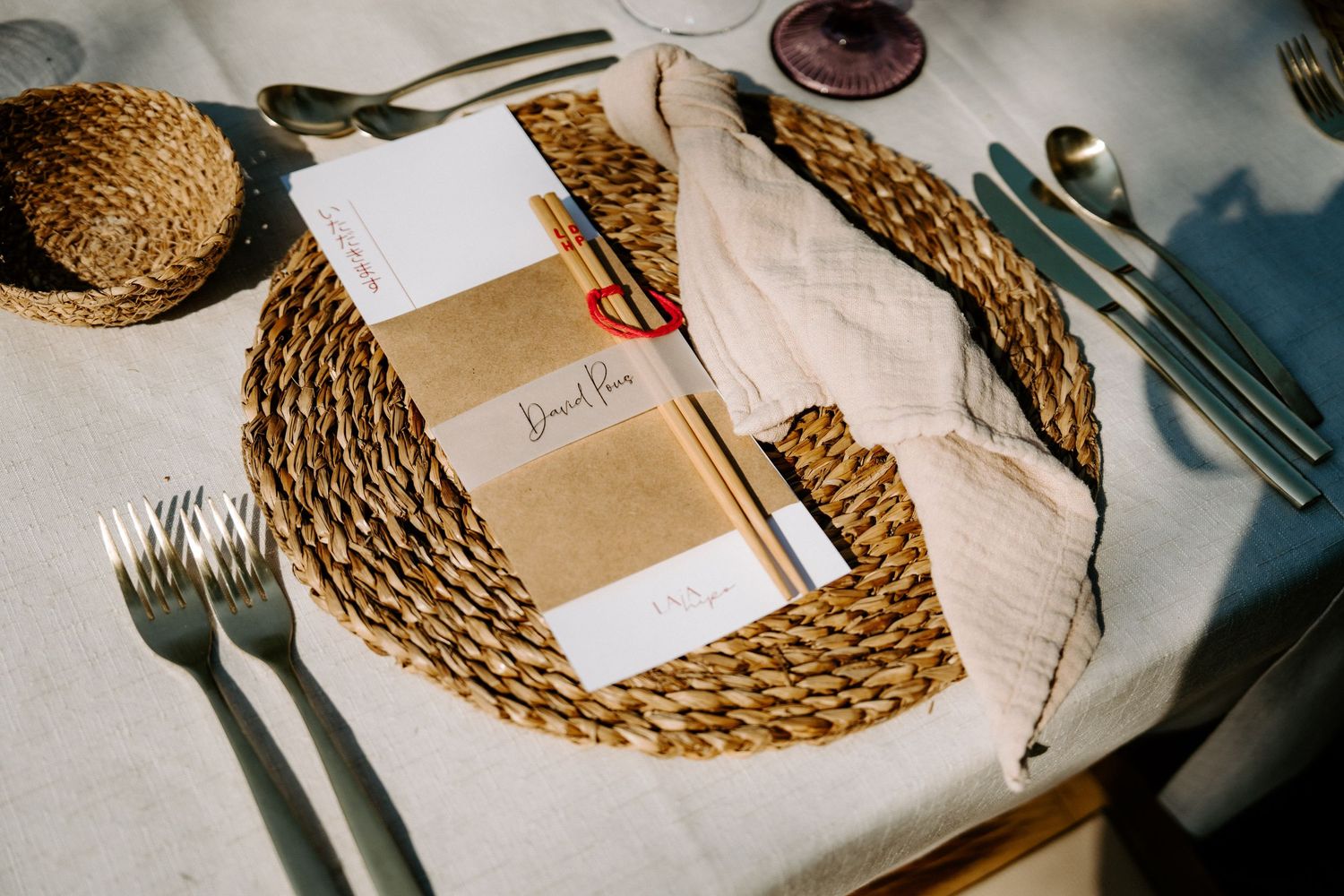 Wedding place setting with woven placemat, menu card, and elegant silverware.