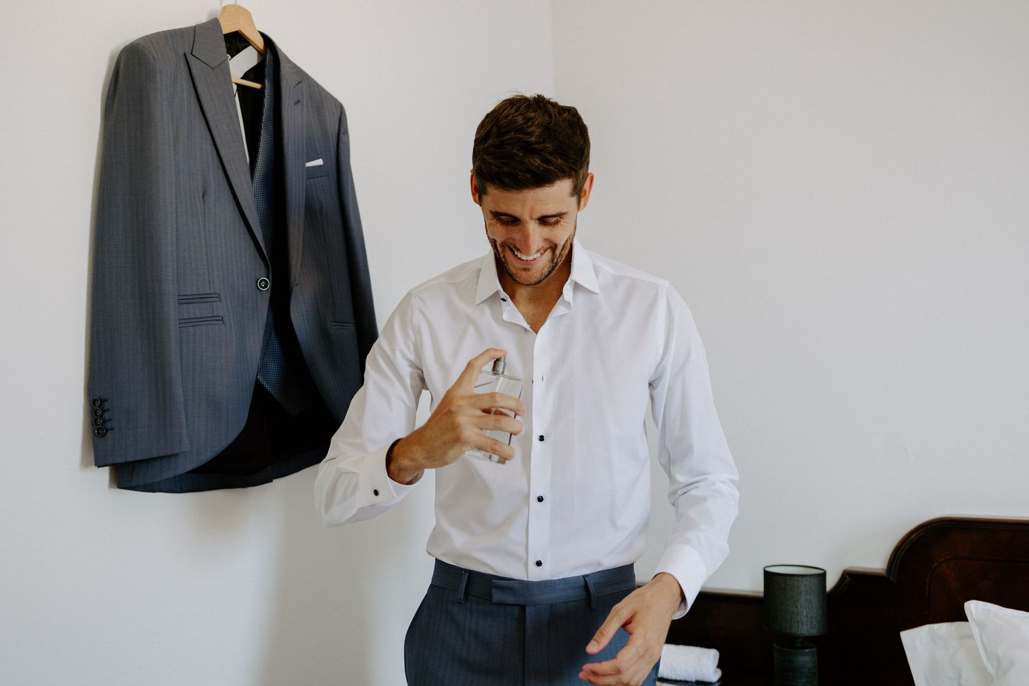 Navy suit jacket hanging on wall while someone adjusts their white dress shirt.