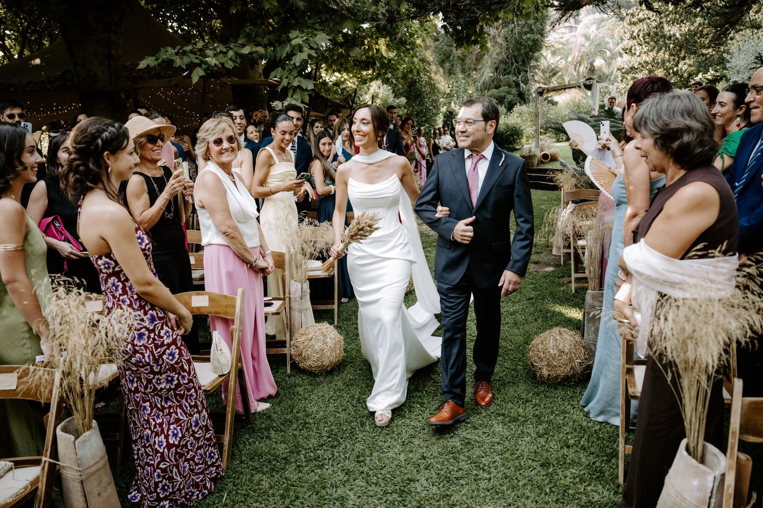 Wedding guests mingle during an outdoor garden ceremony with decorative fans and natural decor.
