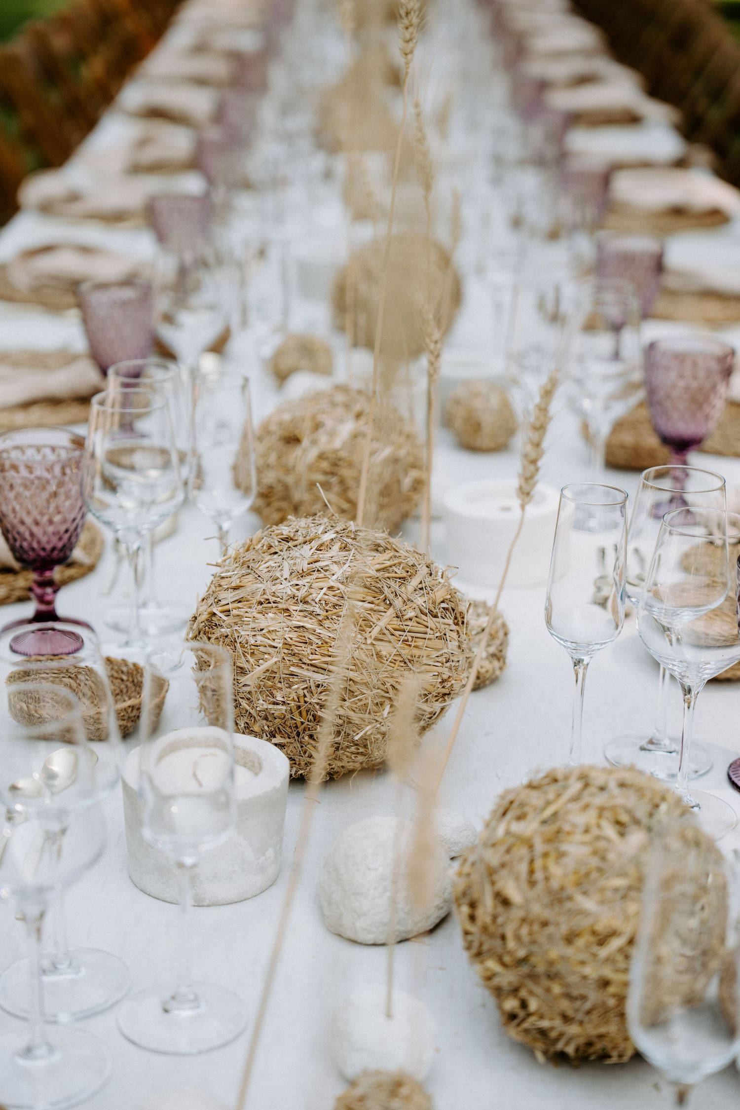 Elegant table setting with rustic hay bale centerpieces and purple glassware at a wedding reception.