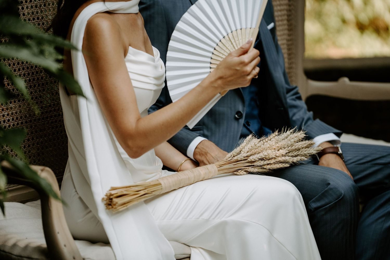 Guests hold decorative white paper fans during an elegant outdoor summer wedding.