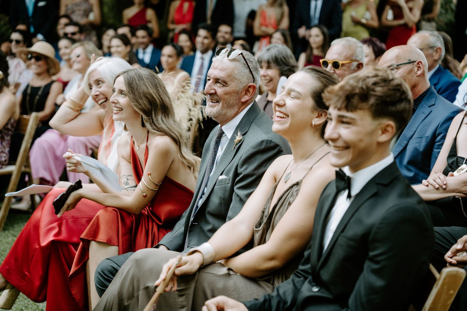 Wedding guests seated in rows watch the ceremony with joyful expressions.