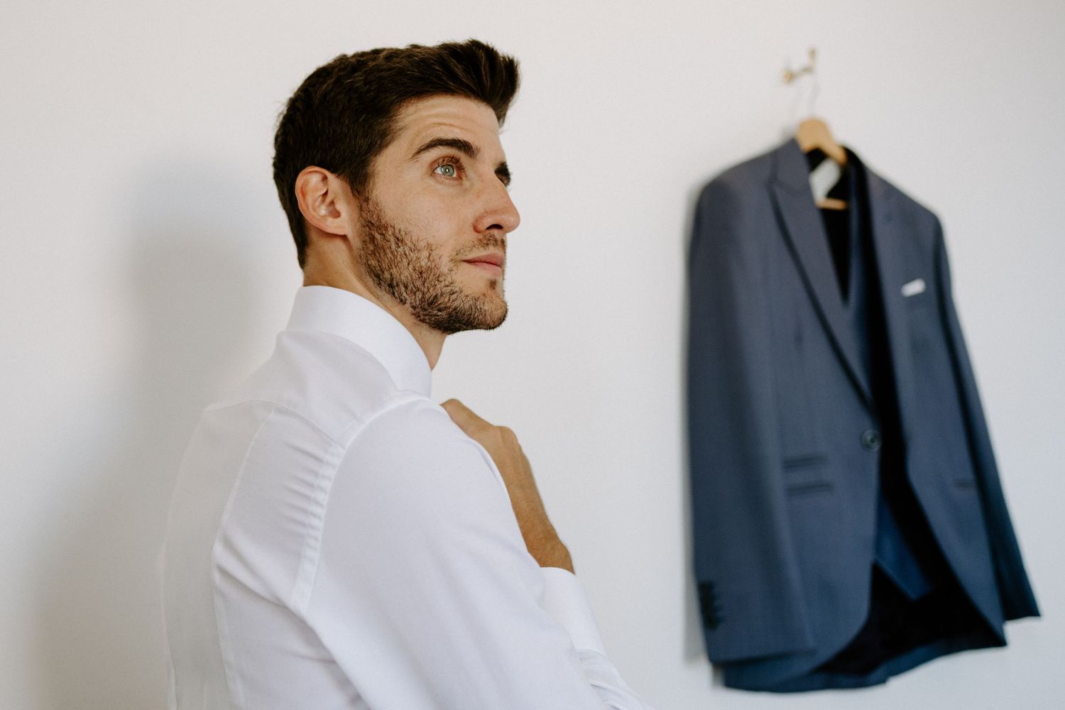 Side profile view of person in white shirt with navy suit hanging in background.