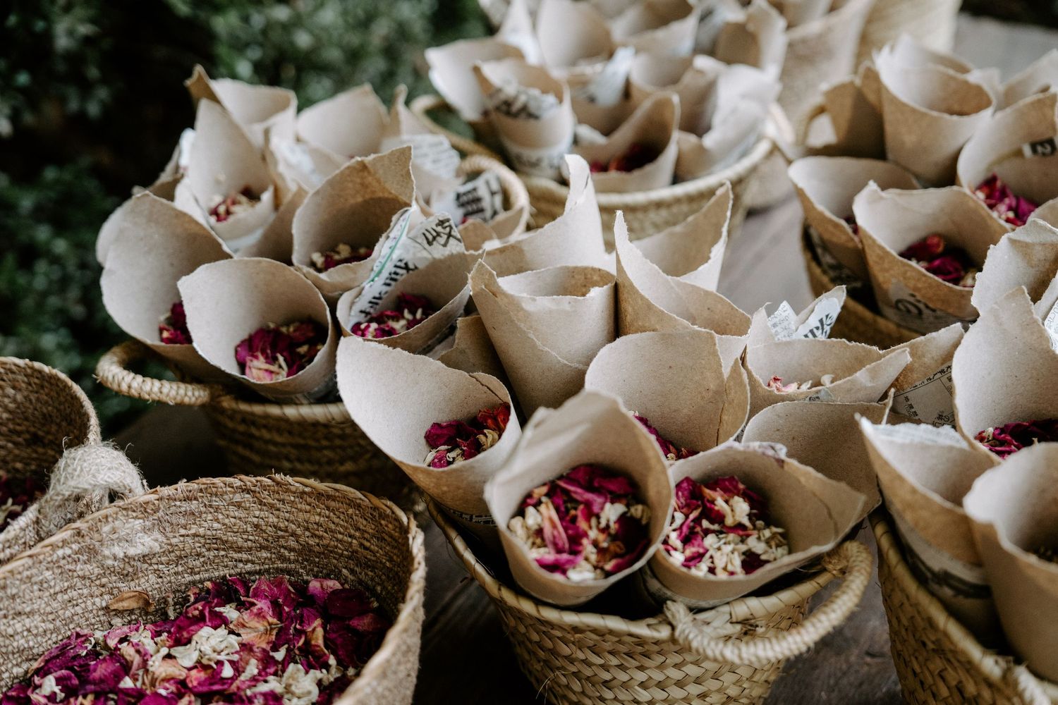 Paper cones filled with flower petals arranged in rustic baskets for wedding toss.