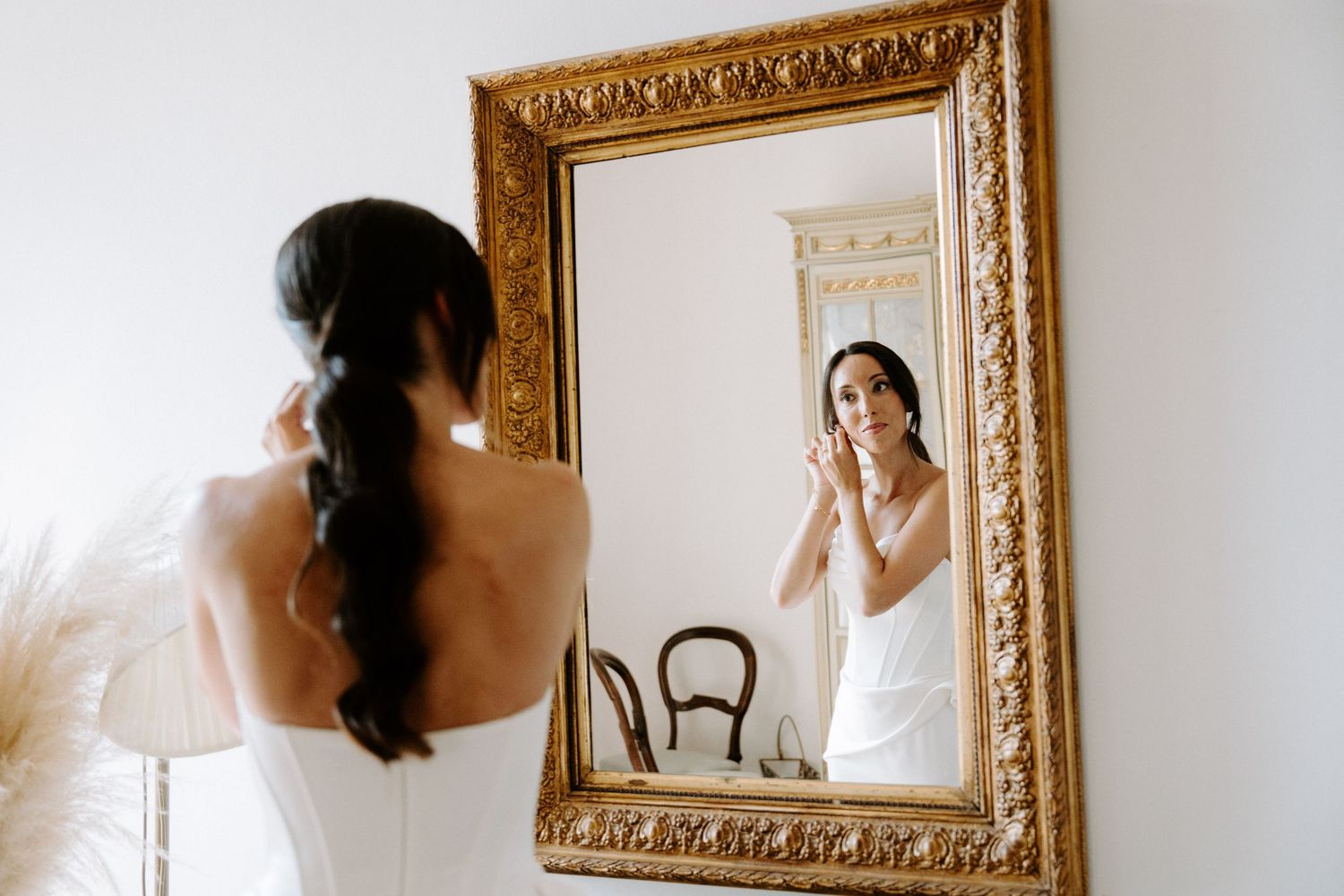 Reflection in ornate gold mirror shows wedding preparation moment.